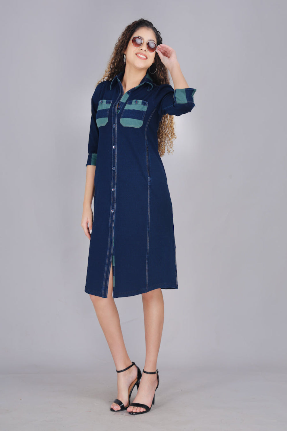 A woman wearing a long denim dress with green and blue striped pockets, button-up front, and two pockets.